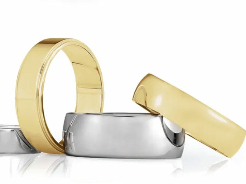 Two gold rings and two silver rings are arranged together on a white surface, with one gold ring resting on top of a silver ring.