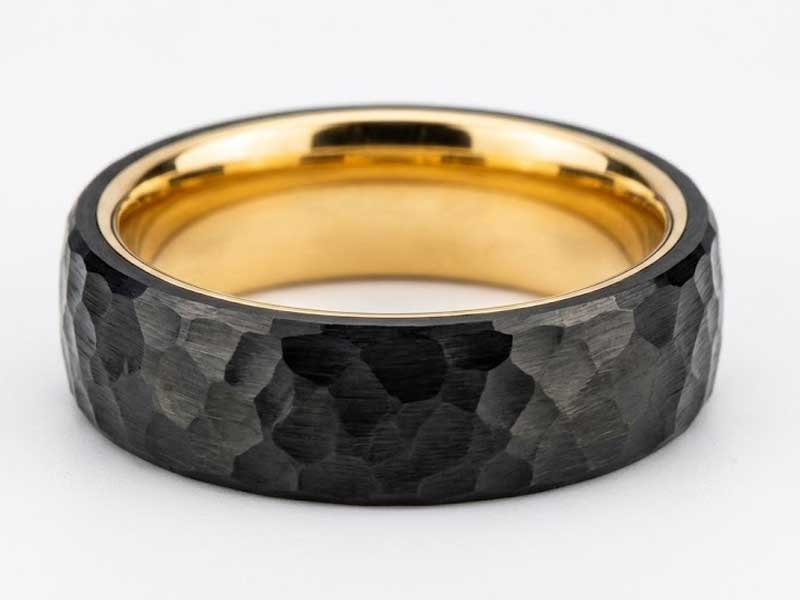 A ring with a faceted black exterior and a smooth, polished gold interior, displayed on a plain white background.