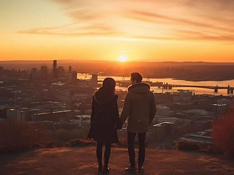 Two people standing on top of a hill overlooking a city at sunset.