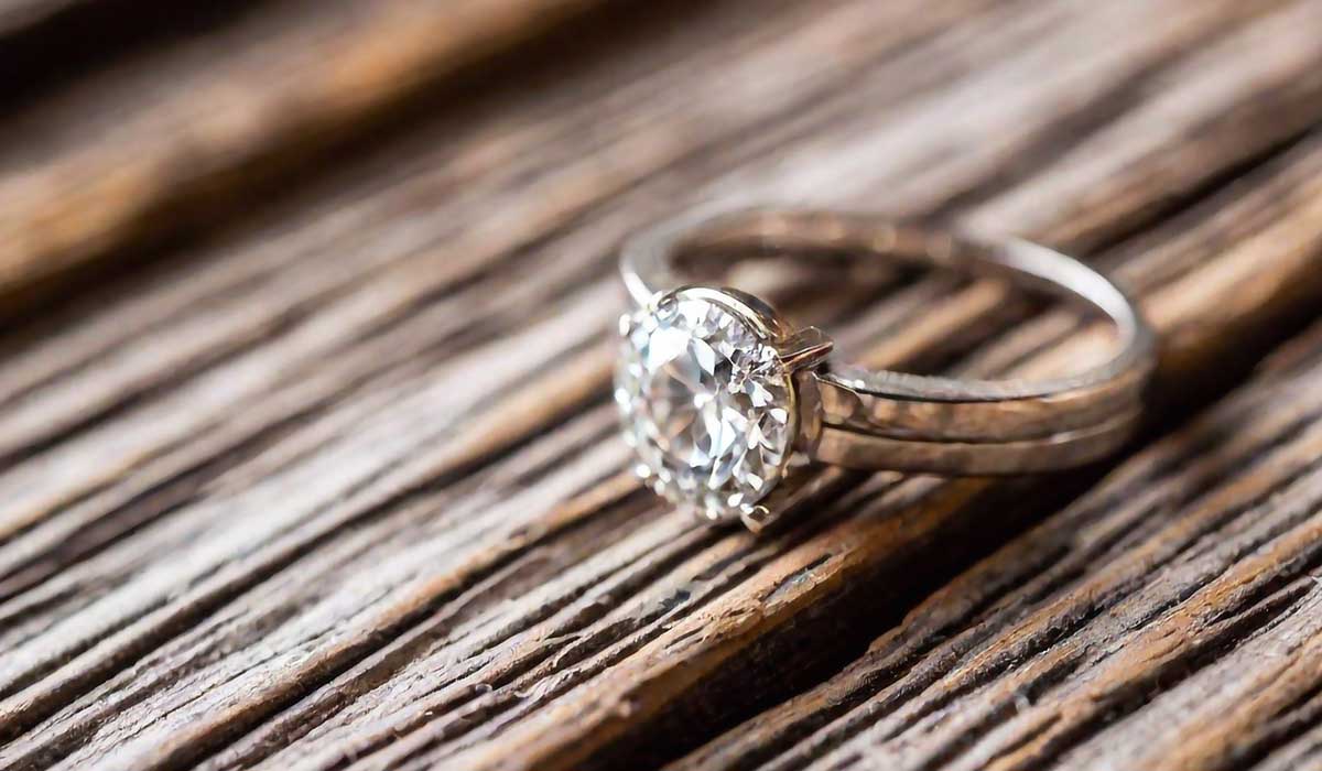 A silver ring with a round, clear gemstone is placed on a textured wooden surface.
