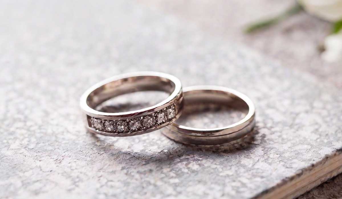 Two silver rings are placed on a textured surface; one ring is plain, and the other is set with small diamonds.