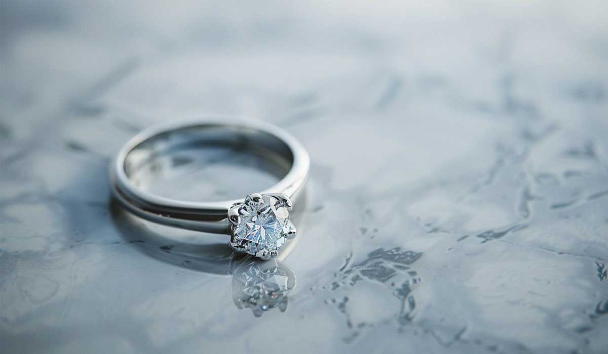 A silver diamond engagement ring rests on a gray marbled surface.