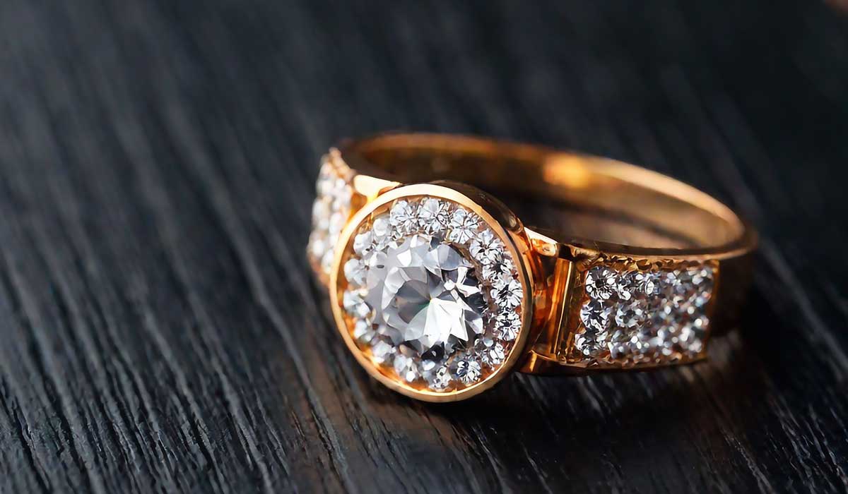 A gold ring with a large central diamond surrounded by smaller diamonds rests on a dark wooden surface.