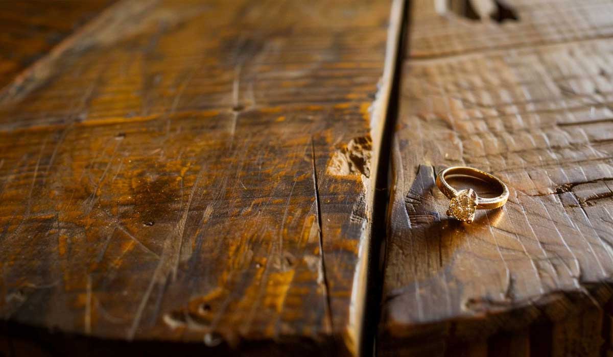 A gold ring with a gemstone rests on a rustic wooden surface with visible grain and cracks.