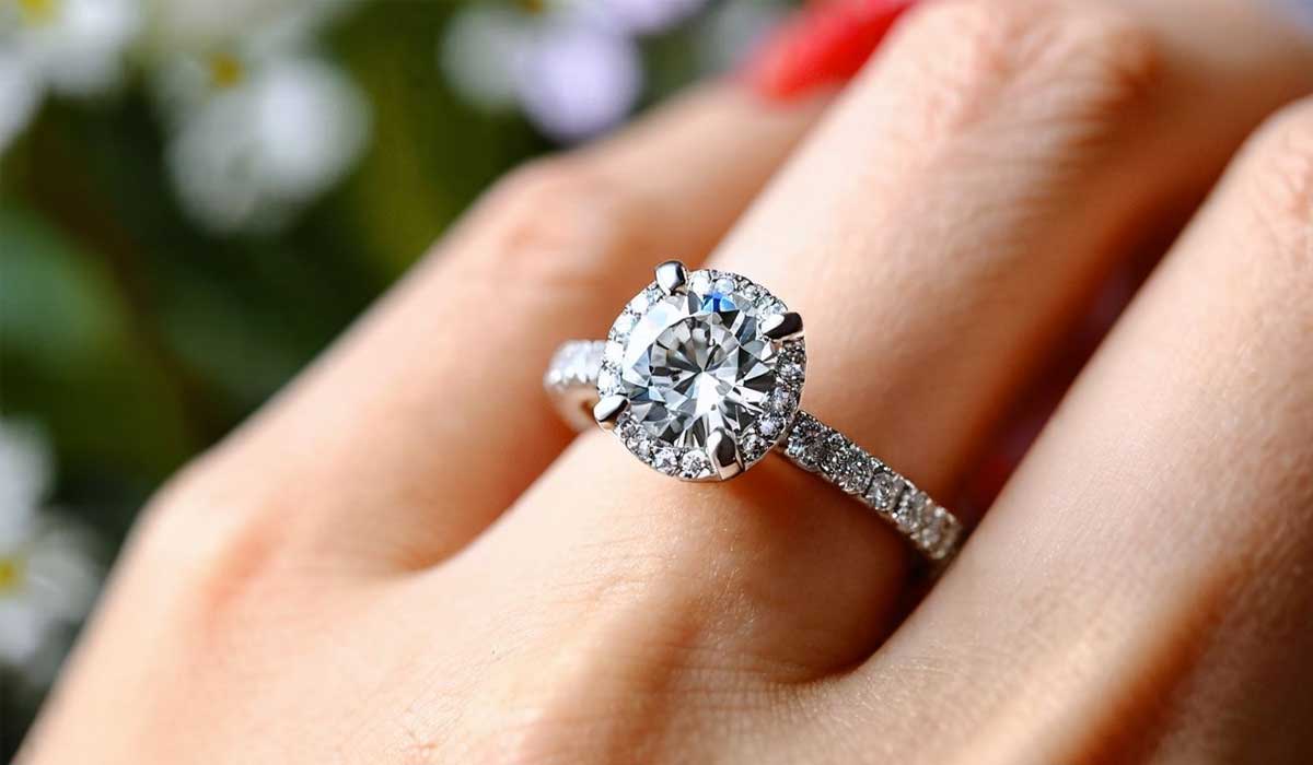 A hand wearing a diamond engagement ring with a large round center stone and a band encrusted with smaller diamonds.