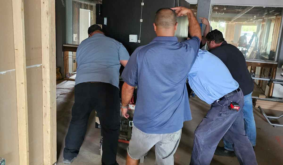Four men are moving a large object on a dolly inside a building under construction or renovation.