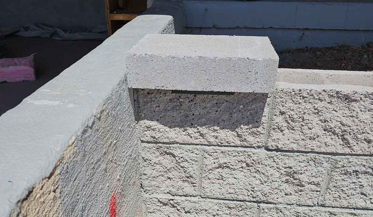 A concrete block rests on top of a partially built cinder block wall at a construction site.
