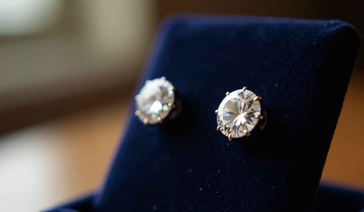 A pair of round diamond stud earrings is displayed on a dark blue velvet stand.