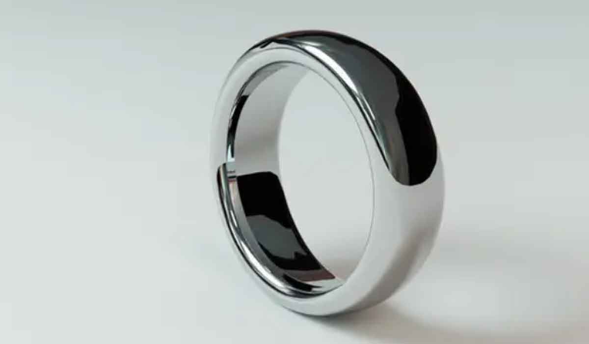 A polished silver ring stands upright on a plain white surface, reflecting light and its surroundings.