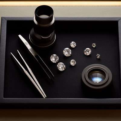 A tray with tweezers, a magnifying loupe, and several cut diamonds arranged neatly on a dark surface.