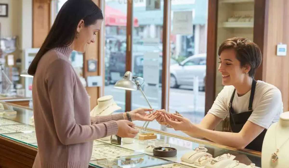 A customer and a saleswoman stand at a jewelry store counter, examining a piece of jewelry together.