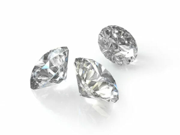 Three clear, faceted diamonds are positioned on a white surface, with each gemstone shown at a different angle.