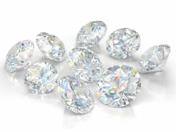 Ten round-cut diamonds are scattered on a white surface, reflecting light and displaying colorful rainbow-like facets.