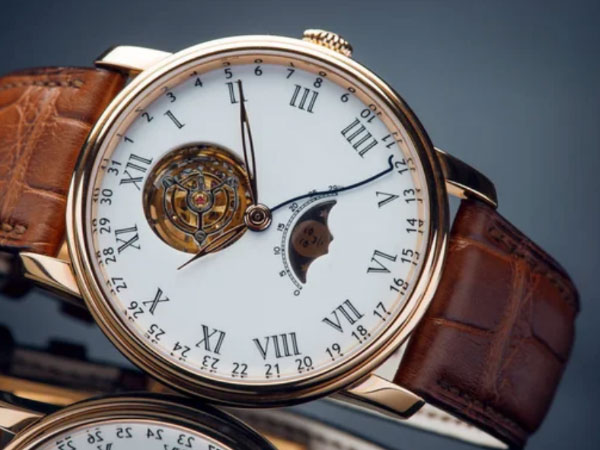 Luxury wristwatch with brown leather band, white dial, Roman numerals, exposed mechanism, and a moon phase indicator.