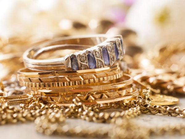 A close-up of stacked gold rings, one with blue stones, surrounded by gold chains and other jewelry.