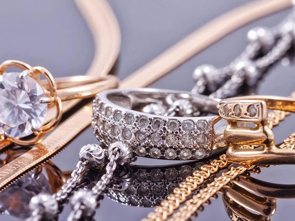 Close-up of assorted gold and silver jewelry, including a diamond ring, chains, and a necklace, displayed on a reflective black surface.