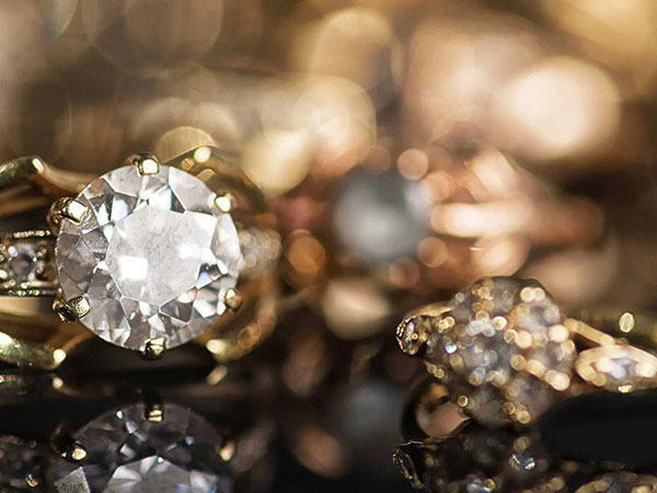 Close-up of a large round diamond set in a gold ring, with other gold jewelry pieces blurred in the background.